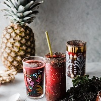 Bright red smoothies in festive glasses with a pineapple in the background