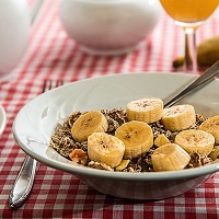 Breakfast bowl of cereal with sliced banana on a red checkered tablecloth