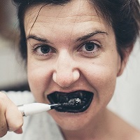 Woman brushing her teeth with charcoal toothpaste