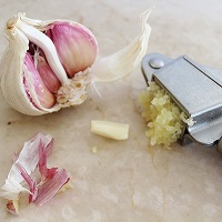 Garlic cloves in garlic crusher next to whole cloves