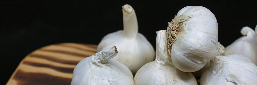 Whole garlic cloves on a wooden chopping board