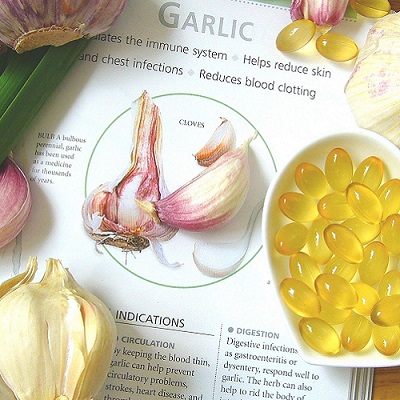 Bowl of garlic oil capsules sitting on a book about the health benefits of garlic
