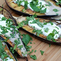 Roasted eggplant drizzled with tahini and sprinkled with green leafy herbs